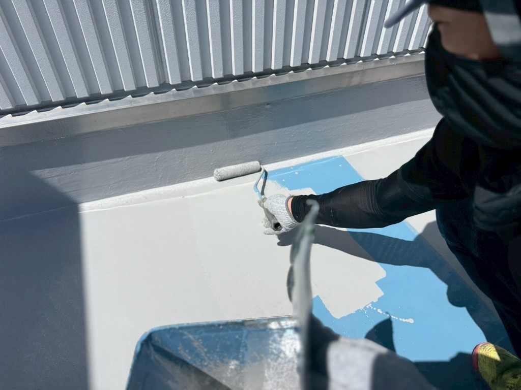 屋上の青系防水層の上にトップコートをローラー施工している様子